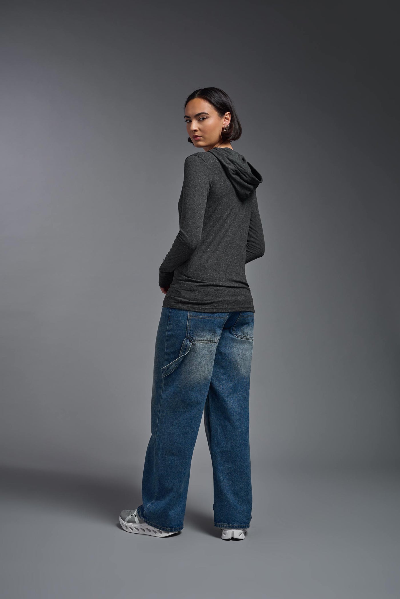 A female model wearing the women's Heather Hoodie Shirt in the color dark heather charcoal, showing the modern fit from a hoodie back view. This hoodie shirt is made in the USA. #color_dark-heather-charcoal