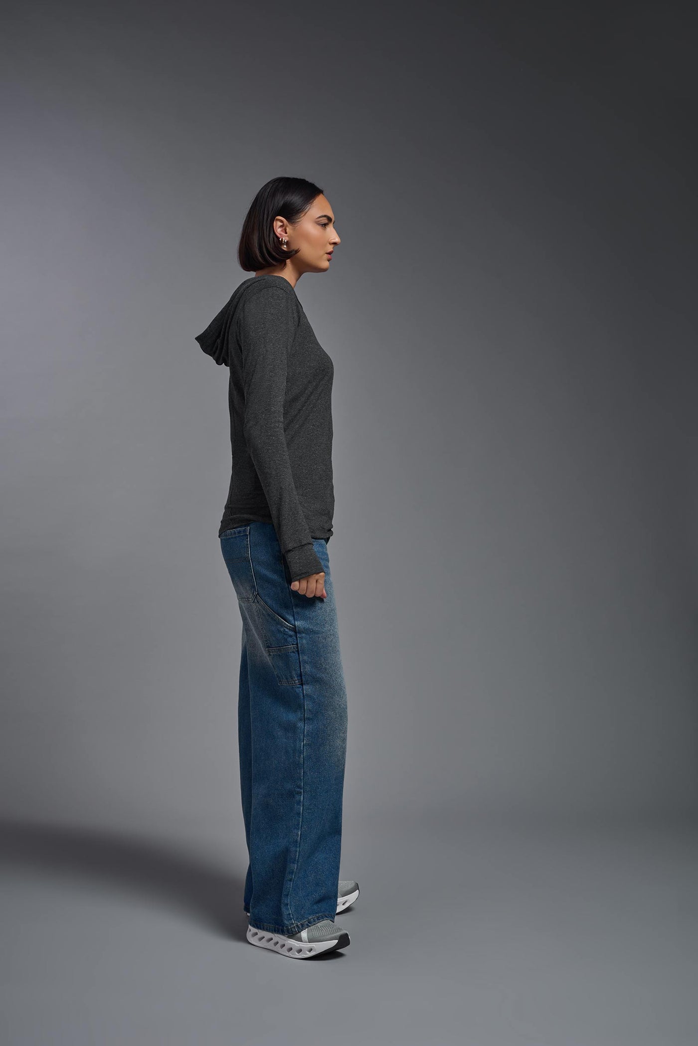 A female model wearing the women's Heather Hoodie Shirt in the color dark heather charcoal, showing the modern fit from a hoodie side view. This hoodie shirt is made in the USA. #color_dark-heather-charcoal
