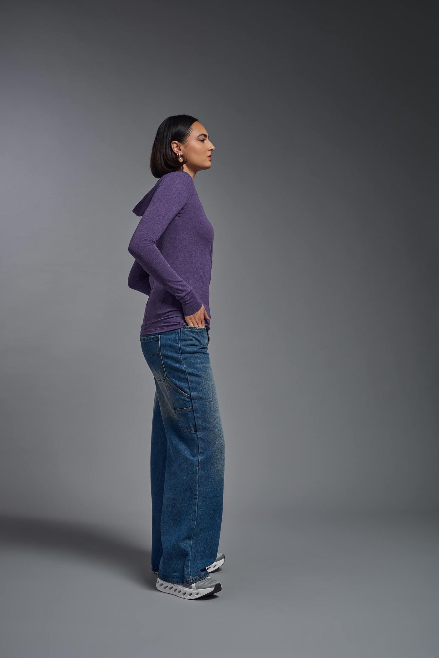 A female model wearing the women's Heather Hoodie Shirt in the color dark heather purple, showing the modern fit from a side view. This hoodie shirt is made in the USA. #color_dark-heather-purple