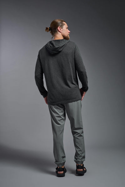 A blonde male model with a beard on a gray background, wearing the men's Heather Hoodie Shirt in the color dark heather charcoal, made out of 88% polyester and 22% treated cotton, showing the relaxed fit from a back view. This hoodie shirt is comfortable and made in the USA. #dark-heather-charcoal