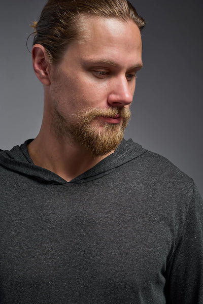 A blonde male model with a beard on a gray background, wearing the men's Heather Hoodie Shirt in the color dark heather charcoal, made out of 88% polyester and 22% treated cotton, showing the relaxed fit from a front closeup collar view. This hoodie shirt is comfortable and made in the USA. #dark-heather-charcoal