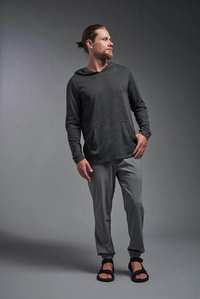 A blonde male model with a beard on a gray background, wearing the men's Heather Hoodie Shirt in the color dark heather charcoal, made out of 88% polyester and 22% treated cotton, showing the relaxed fit from a front view. This hoodie shirt is comfortable and made in the USA. #dark-heather-charcoal