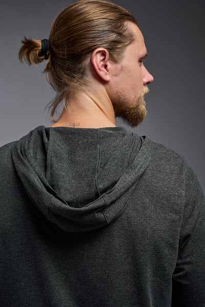 A blonde male model with a beard on a gray background, wearing the men's Heather Hoodie Shirt in the color dark heather charcoal, made out of 88% polyester and 22% treated cotton, showing the relaxed fit from a back closeup hood view. This hoodie shirt is comfortable and made in the USA. #dark-heather-charcoal