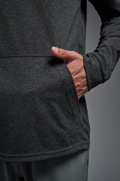 A blonde male model with a beard on a gray background, wearing the men's Heather Hoodie Shirt in the color dark heather charcoal, made out of 88% polyester and 22% treated cotton, showing the relaxed fit from a closeup pocket view. This hoodie shirt is comfortable and made in the USA. #dark-heather-charcoal