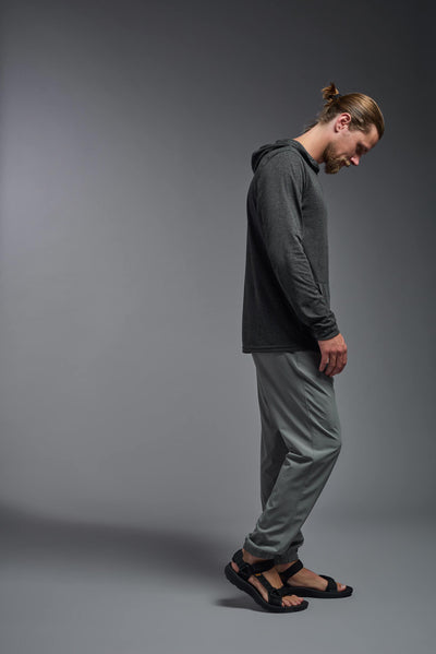 A blonde male model with a beard on a gray background, wearing the men's Heather Hoodie Shirt in the color dark heather charcoal, made out of 88% polyester and 22% treated cotton, showing the relaxed fit from a side view. This hoodie shirt is comfortable and made in the USA. #dark-heather-charcoal