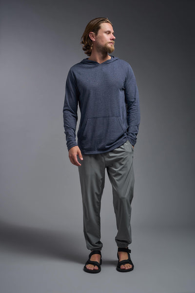 A blonde male model with a beard on a gray background, wearing the men's Heather Hoodie Shirt in the color dark heather navy, made out of 88% polyester and 22% treated cotton, showing the relaxed fit from a front view. This hoodie shirt is comfortable and made in the USA. #dark-heather-navy