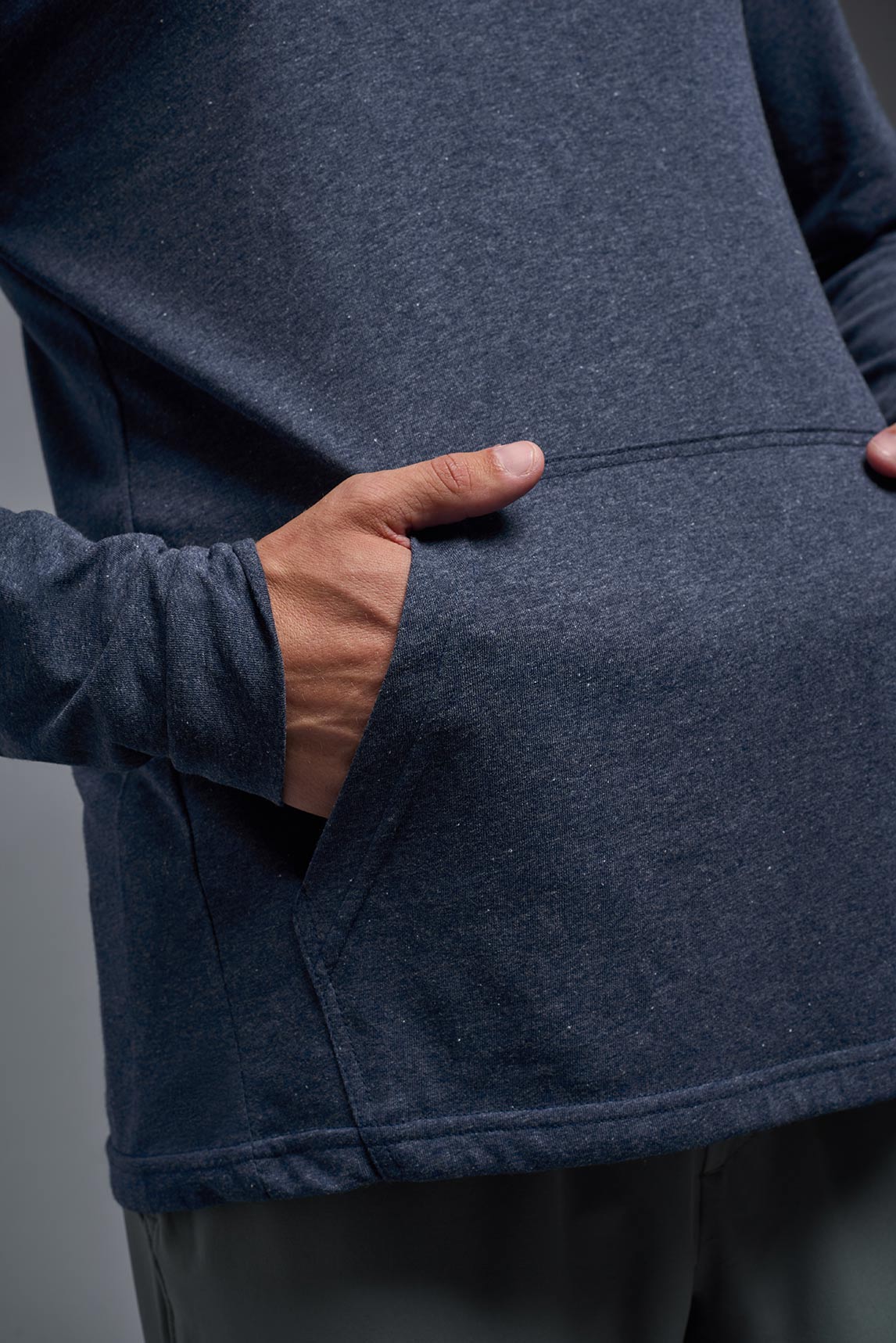 A blonde male model with a beard on a gray background, wearing the men's Heather Hoodie Shirt in the color dark heather navy, made out of 88% polyester and 22% treated cotton, showing the relaxed fit from a front closeup pocket view. This hoodie shirt is comfortable and made in the USA. #dark-heather-navy