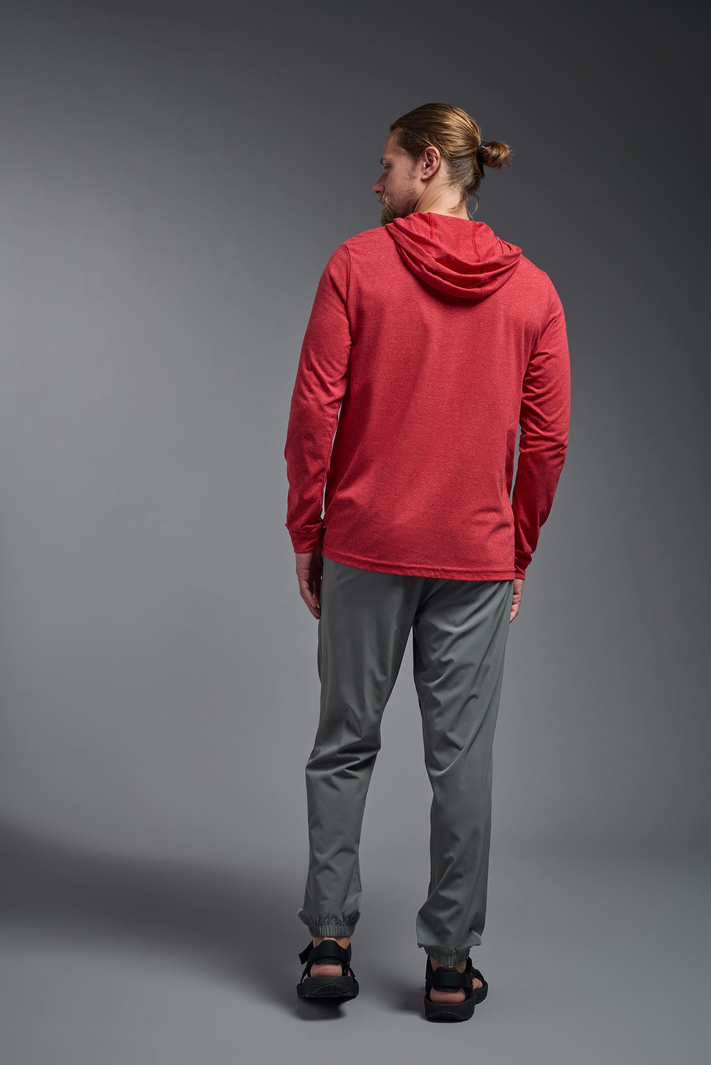 A blonde male model with a beard on a gray background, wearing the men's Heather Hoodie Shirt in the color dark heather red, made out of 88% polyester and 22% treated cotton, showing the relaxed fit from a back view. This hoodie shirt is comfortable and made in the USA. #dark-heather-red