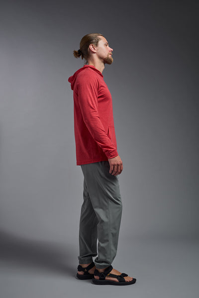 A blonde male model with a beard on a gray background, wearing the men's Heather Hoodie Shirt in the color dark heather red, made out of 88% polyester and 22% treated cotton, showing the relaxed fit from a side view. This hoodie shirt is comfortable and made in the USA. #dark-heather-red