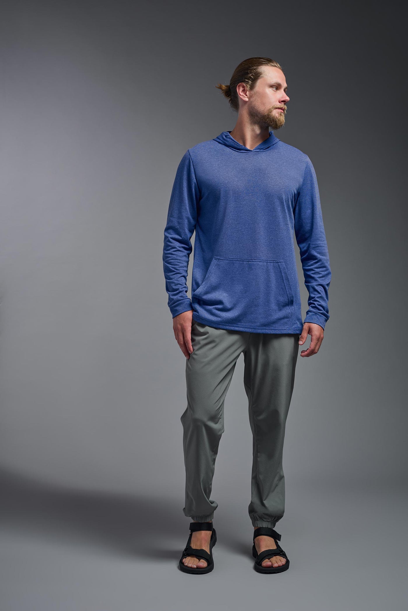 A blonde male model with a beard on a gray background, wearing the men's Heather Hoodie Shirt in the color dark heather royal, made out of 88% polyester and 22% treated cotton, showing the relaxed fit from a front view. This hoodie shirt is comfortable and made in the USA. #dark-heather-royal