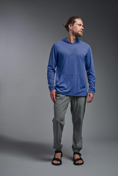 A blonde male model with a beard on a gray background, wearing the men's Heather Hoodie Shirt in the color dark heather royal, made out of 88% polyester and 22% treated cotton, showing the relaxed fit from a front view. This hoodie shirt is comfortable and made in the USA. #dark-heather-royal