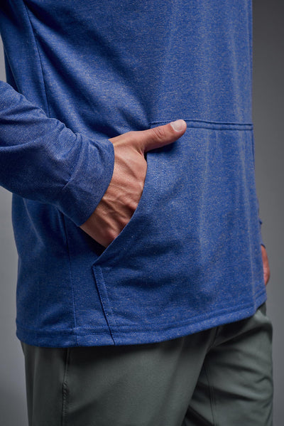 A blonde male model with a beard on a gray background, wearing the men's Heather Hoodie Shirt in the color dark heather royal, made out of 88% polyester and 22% treated cotton, showing the relaxed fit from a front closeup pocket view. This hoodie shirt is comfortable and made in the USA. #dark-heather-royal