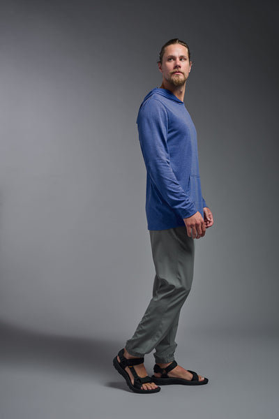 A blonde male model with a beard on a gray background, wearing the men's Heather Hoodie Shirt in the color dark heather royal, made out of 88% polyester and 22% treated cotton, showing the relaxed fit from a side view. This hoodie shirt is comfortable and made in the USA. #dark-heather-royal
