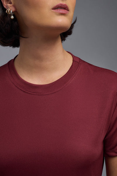 A female model with short brown hair on a gray background, wearing the Women's DriMax Crewneck Expert Tee in the color cardinal from a closeup collar front view. This shirt is made in the USA and is quick-drying and moisture-wicking. #color_cardinal