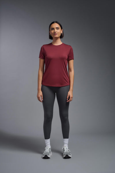 A female model with short brown hair on a gray background, wearing the Women's DriMax Crewneck Expert Tee in the color cardinal from a full body front view. This shirt is made in the USA and is quick-drying and moisture-wicking. #color_cardinal