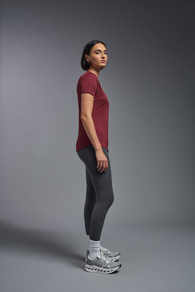 A female model with short brown hair on a gray background, wearing the Women's DriMax Crewneck Expert Tee in the color cardinal from a full body side view. This shirt is made in the USA and is quick-drying and moisture-wicking. #color_cardinal