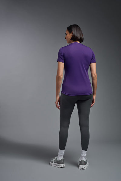 A female model with short brown hair on a gray background, wearing the Women's DriMax Crewneck Expert Tee in the color dark purple from a full body back view. This shirt is made in the USA and is quick-drying and moisture-wicking. #color_dark-purple