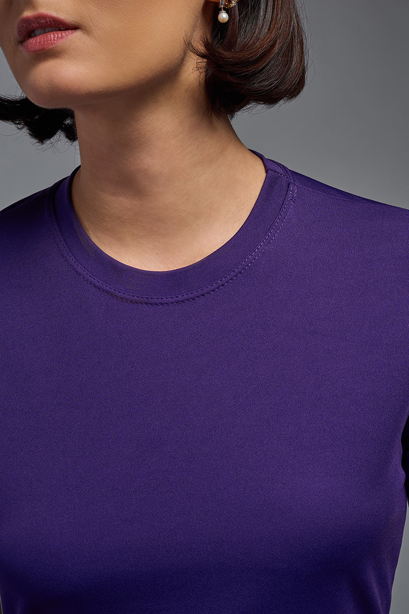 A female model with short brown hair on a gray background, wearing the Women's DriMax Crewneck Expert Tee in the color dark purple from a closeup collar front view. This shirt is made in the USA and is quick-drying and moisture-wicking. #color_dark-purple