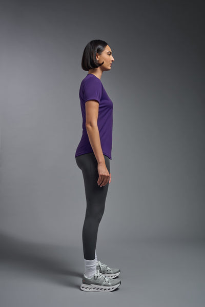 A female model with short brown hair on a gray background, wearing the Women's DriMax Crewneck Expert Tee in the color dark purple from a full body side view. This shirt is made in the USA and is quick-drying and moisture-wicking. #color_dark-purple
