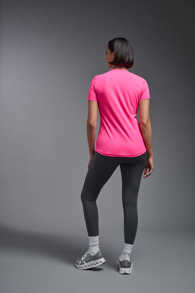 A female model with short brown hair on a gray background, wearing the Women's DriMax Crewneck Expert Tee in the color hot pink from a full body back view. This shirt is made in the USA and is quick-drying and moisture-wicking. #color_hot-pink