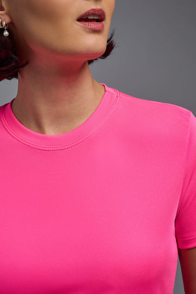 A female model with short brown hair on a gray background, wearing the Women's DriMax Crewneck Expert Tee in the color hot pink from a closeup collar front view. This shirt is made in the USA and is quick-drying and moisture-wicking. #color_hot-pink