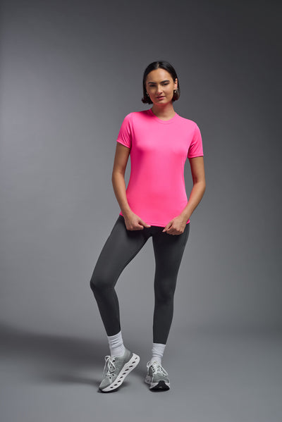 A female model with short brown hair on a gray background, wearing the Women's DriMax Crewneck Expert Tee in the color hot pink from a full body front view. This shirt is made in the USA and is quick-drying and moisture-wicking. #color_hot-pink
