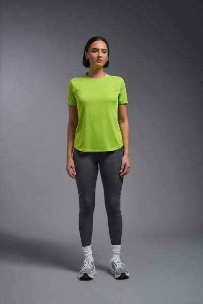 A female model with short brown hair on a gray background, wearing the Women's DriMax Crewneck Expert Tee in the color key lime from a full body front view. This shirt is made in the USA and is quick-drying and moisture-wicking. #color_key-lime