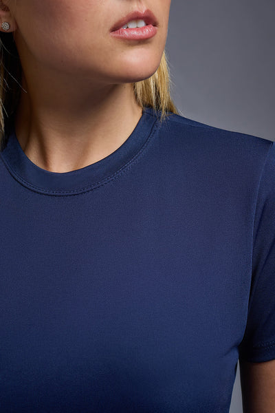 A female model with blonde straight hair on a gray background, wearing the Women's DriMax Crewneck Expert Tee in the color navy from a closeup collar front view. This shirt is made in the USA and is quick-drying and moisture-wicking. #color_navy