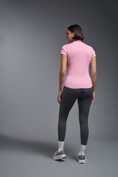 A female model with short brown hair on a gray background, wearing the Women's DriMax Crewneck Expert Tee in the color pink from a full body back view. This shirt is made in the USA and is quick-drying and moisture-wicking. #color_pink