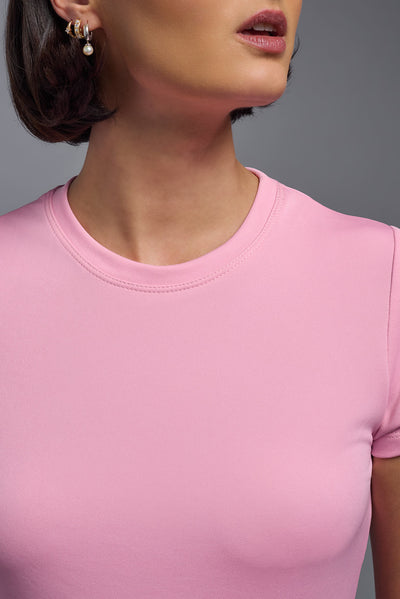 A female model with short brown hair on a gray background, wearing the Women's DriMax Crewneck Expert Tee in the color pink from a closeup collar front view. This shirt is made in the USA and is quick-drying and moisture-wicking. #color_pink