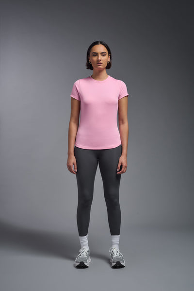 A female model with short brown hair on a gray background, wearing the Women's DriMax Crewneck Expert Tee in the color pink from a full body front view. This shirt is made in the USA and is quick-drying and moisture-wicking. #color_pink
