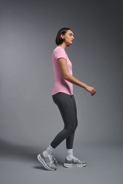 A female model with short brown hair on a gray background, wearing the Women's DriMax Crewneck Expert Tee in the color pink from a full body side view. This shirt is made in the USA and is quick-drying and moisture-wicking. #color_pink