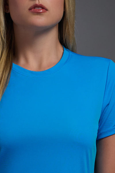 A female model with blonde straight hair on a gray background, wearing the Women's DriMax Crewneck Expert Tee in the color safety blue from a closeup collar front view. This shirt is made in the USA and is quick-drying and moisture-wicking. #color_safety-blue