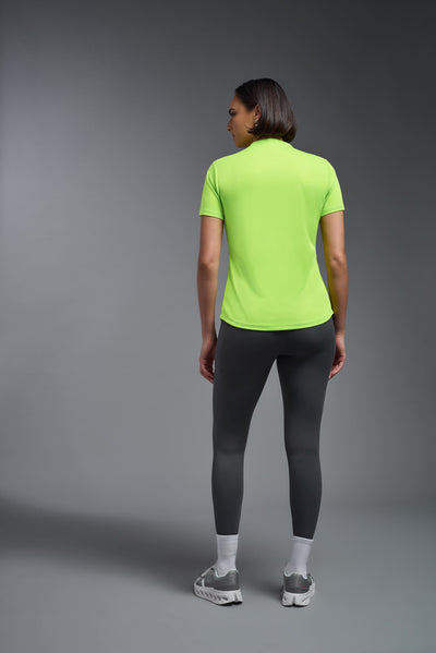 A female model with short brown hair on a  gray background, wearing the Women's DriMax Crewneck Expert Tee in the color safety yellow from a full body back view. This shirt is made in the USA and is quick-drying and moisture-wicking. #color_safety-yellow