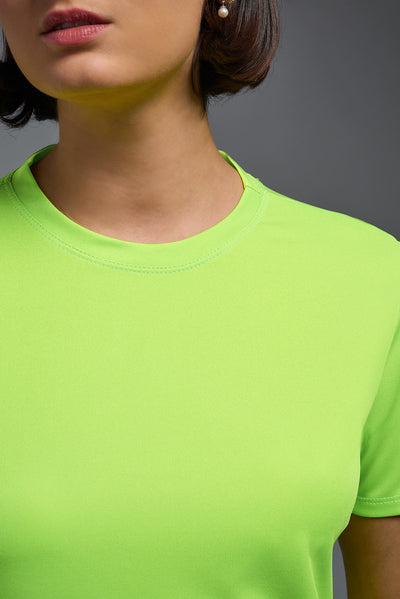 A female model with short brown hair on a gray background, wearing the Women's DriMax Crewneck Expert Tee in the color safety yellow from a closeup collar front view. This shirt is made in the USA and is quick-drying and moisture-wicking. #color_safety-yellow