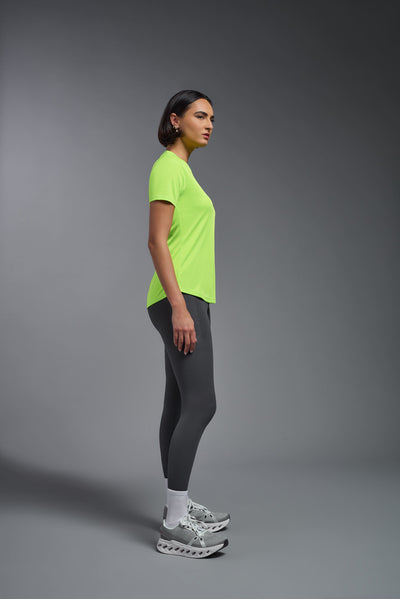 A female model with short brown hair on a gray background, wearing the Women's DriMax Crewneck Expert Tee in the color safety yellow from a full body side view. This shirt is made in the USA and is quick-drying and moisture-wicking. #color_safety-yellow