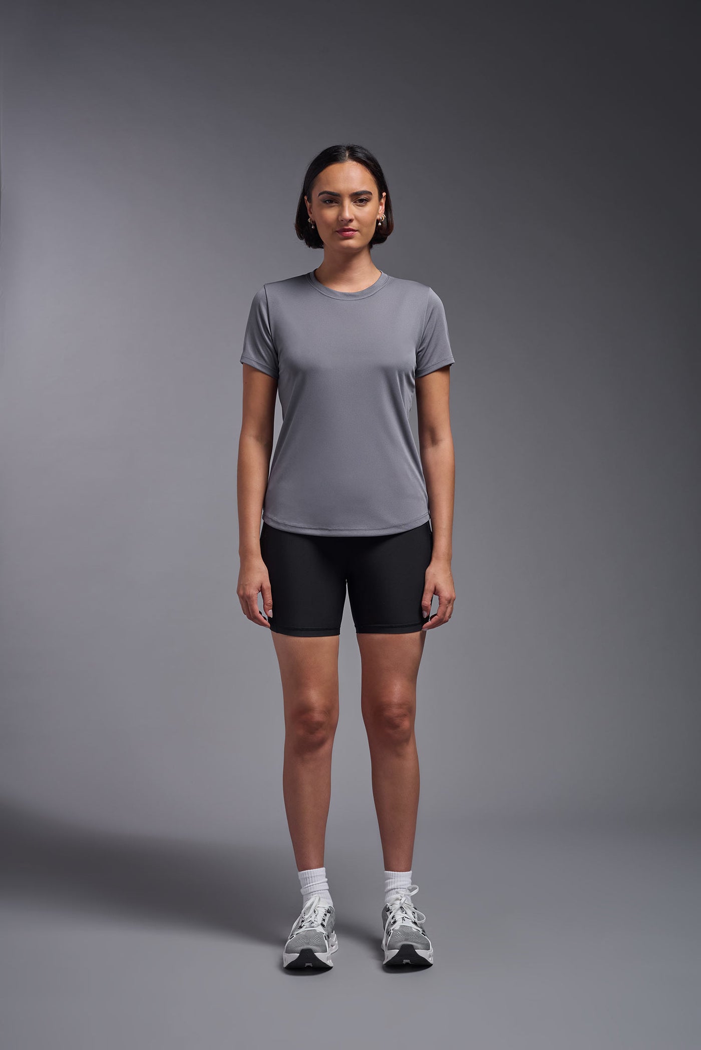 A female model with short brown hair on a gray background, wearing the Women's DriMax Crewneck Expert Tee in the color steel gray from a front view. This shirt is made in the USA and is quick-drying and moisture-wicking. #color_steel