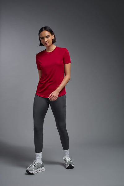 A female model with short brown hair on a gray background, wearing the Women's DriMax Crewneck Expert Tee in the color true red from a full body front view. This shirt is made in the USA and is quick-drying and moisture-wicking. #color_red