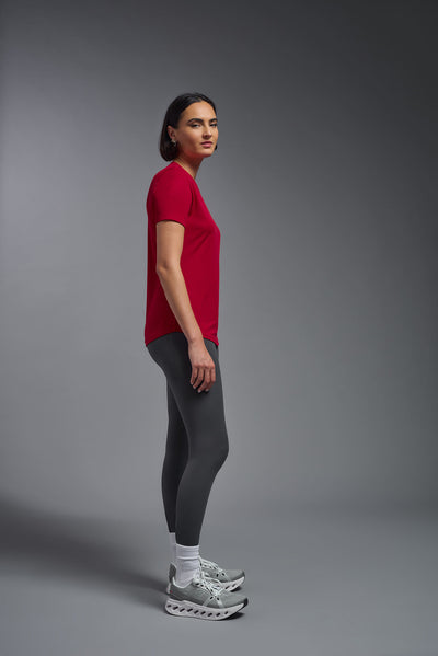 A female model with short brown hair on a gray background, wearing the Women's DriMax Crewneck Expert Tee in the color true red from a full body side view. This shirt is made in the USA and is quick-drying and moisture-wicking. #color_red