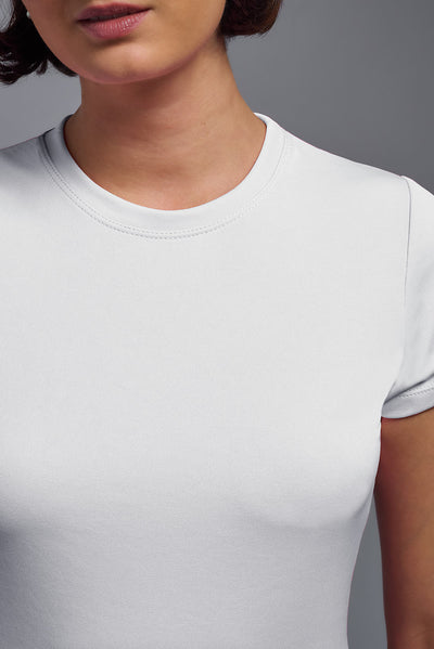A female model with short brown hair on a gray background, wearing the Women's DriMax Crewneck Expert Tee in the color white from a closeup collar view. This shirt is made in the USA and is quick-drying and moisture-wicking. #color_white