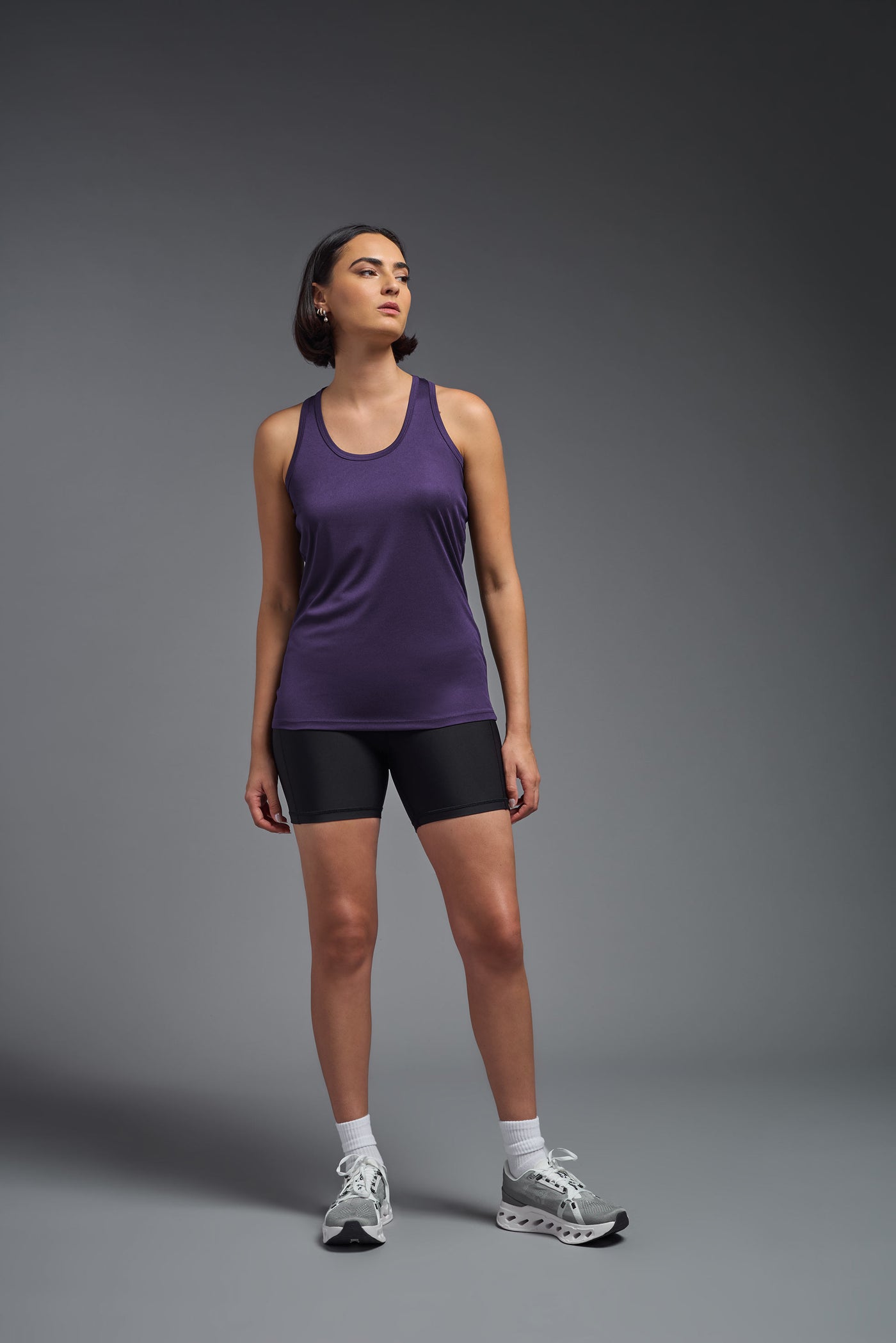 A female model with brown short hair on a gray background, wearing the Women's DrImax Endurance Racerback Tank in the color dark purple from a full body front view. This tank is made in the USA and is quick-drying and moisture-wicking. #color_dark-purple