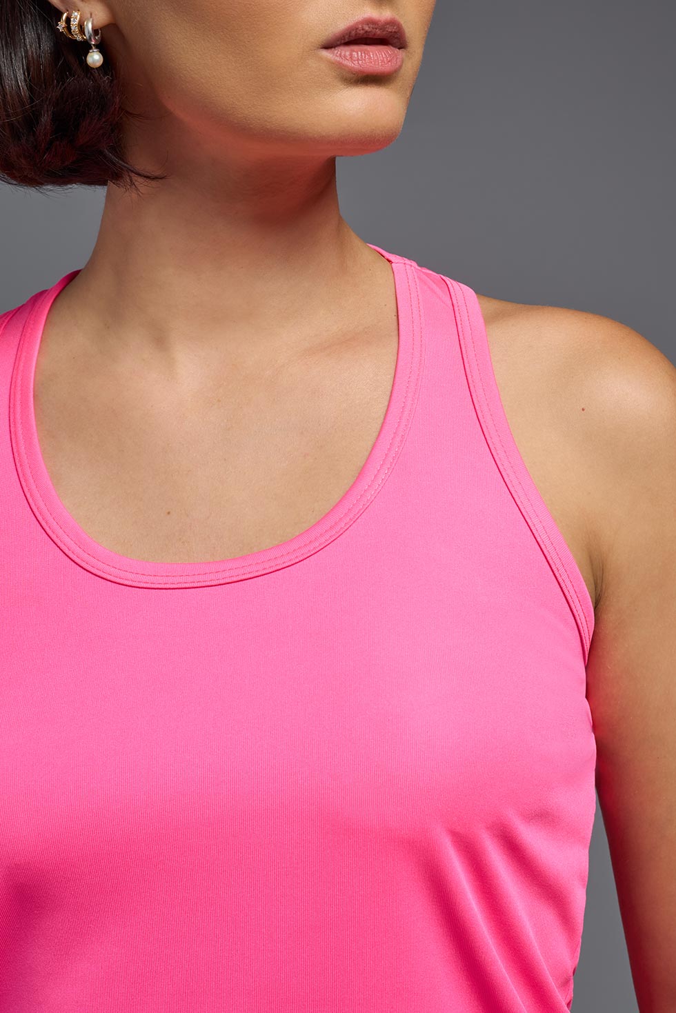 A female model with brown short hair on a gray background, wearing the Women's DrImax Endurance Racerback Tank in the color hot pink from a full body collar view. This tank is made in the USA and is quick-drying and moisture-wicking. #color_hot-pink