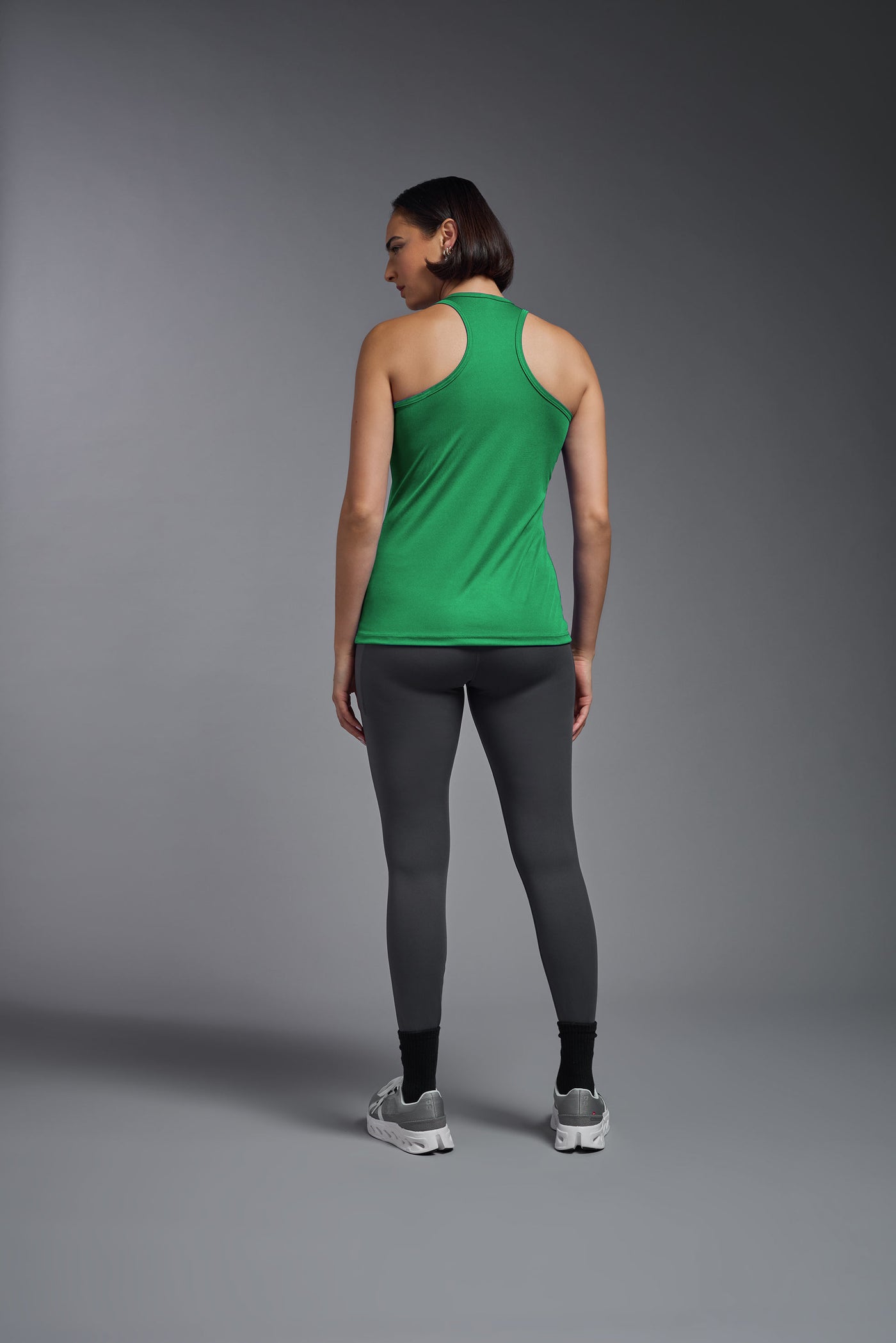 A female model with brown short hair on a gray background, wearing the Women's DrImax Endurance RacerbackTank in the color kelly green from a full body back view. This tank is made in the USA and is quick-drying and moisture-wicking. #color_kelly