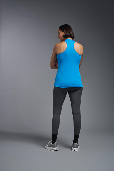 A female model with brown short hair on a gray background, wearing the Women's DrImax Endurance Racerback Tank in the color safety blue from a full body back view. This tank is made in the USA and is quick-drying and moisture-wicking. #color_safety-blue