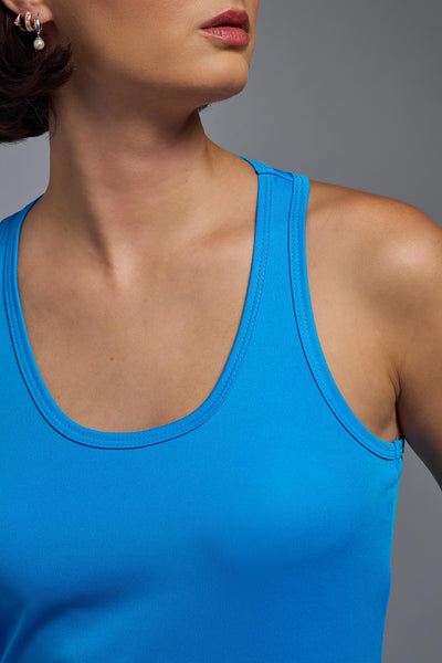A female model with brown short hair on a gray background, wearing the Women's DrImax Endurance Racerback Tank in the color safety blue from a front collar view. This tank is made in the USA and is quick-drying and moisture-wicking. #color_safety-blue