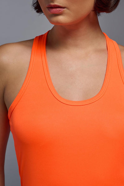 A female model with brown short hair on a gray background, wearing the Women's DrImax Endurance Racerback Tank in the color safety orange from a full body collar view. This tank is made in the USA and is quick-drying and moisture-wicking. #color_safety-orange