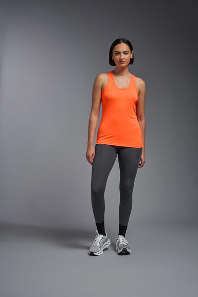 A female model with brown short hair on a gray background, wearing the Women's DrImax Endurance Racerback Tank in the color safety orange from a full body front view. This tank is made in the USA and is quick-drying and moisture-wicking. #color_safety-orange