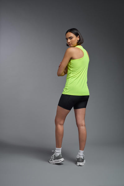 A female model with brown short hair on a gray background, wearing the Women's DrImax Endurance racerback Tank in the color safety yellow from a full body back view. This tank is made in the USA and is quick-drying and moisture-wicking. #color_safety-yellow