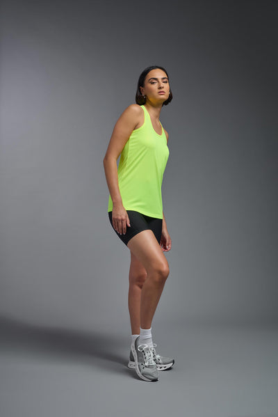 A female model with brown short hair on a gray background, wearing the Women's DrImax Endurance Racerback Tank in the color safety yellow from a full body side view. This tank is made in the USA and is quick-drying and moisture-wicking. #color_safety-yellow