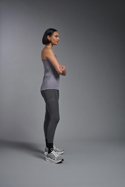 A female model with brown short hair on a gray background, wearing the Women's Drimax Endurance Racerback Tank in the color steel from a full body side view. This tank is made in the USA and is quick-drying and moisture-wicking. #color_steel